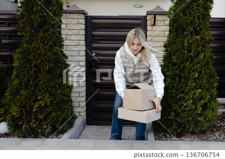 Woman picking up delivered cardboard boxes in front of her house Woman picking up delivered cardboard boxes in front of her house 136706754