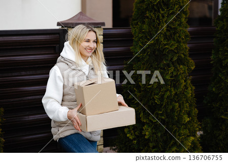 Woman carrying cardboard boxes entering her house garden Woman carrying cardboard boxes entering her house garden 136706755