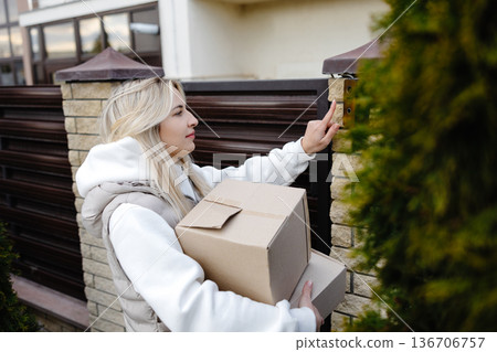 Delivery woman ringing doorbell while holding parcel Delivery woman ringing doorbell while holding parcel 136706757