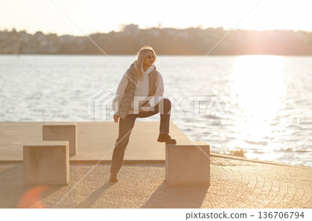 Young woman posing on concrete block by the lake at sunset 136706794