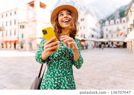 Young woman in a green dress smiles while using her yellow smartphone. Travel, tourism, technology 136707047