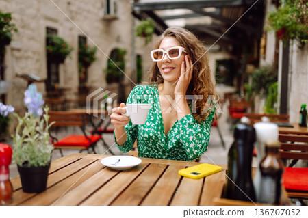 Happy young woman drinking tea, coffee while sitting in a Cafe. People, fashion, lifestyle Happy young woman drinking tea, coffee while sitting in a Cafe. People, fashion, lifestyle 136707052