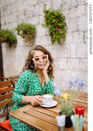 Happy young woman drinking tea, coffee while sitting in a Cafe. People, fashion, lifestyle Happy young woman drinking tea, coffee while sitting in a Cafe. People, fashion, lifestyle 136707053
