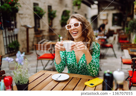 Happy young woman drinking tea, coffee while sitting in a Cafe. People, fashion, lifestyle Happy young woman drinking tea, coffee while sitting in a Cafe. People, fashion, lifestyle 136707055