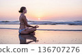 Woman meditating on beach during serene sunset 136707276