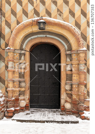 Weathered facade with an old black metal arched door 136707383