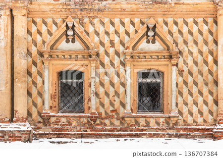 Weathered historic facade with two ornate windows 136707384