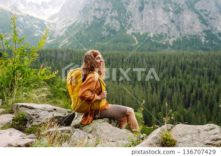 Young traveler woman with a yellow backpack on a cliff. Sports concept, traveler. Active lifestyle. 136707429