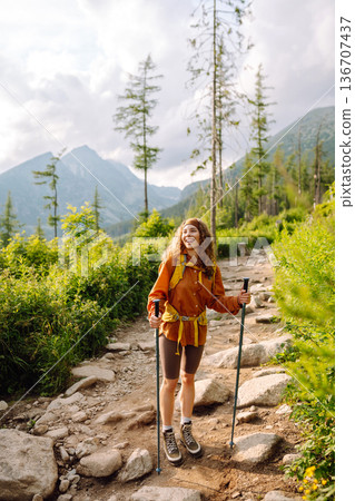 Young woman traveler hiking poles on trail among the mountains. Hiking. Active lifestyle. Young woman traveler hiking poles on trail among the mountains. Hiking. Active lifestyle. 136707437