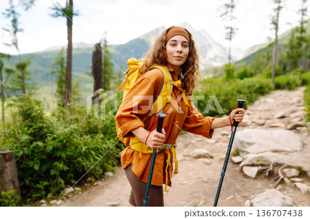 Young woman traveler hiking poles on trail among the mountains. Hiking. Active lifestyle. 136707438