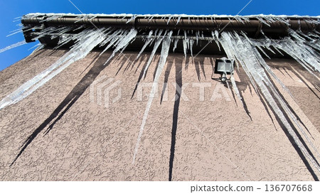 Icicles of ice hang from a roof gutter and a floodlight 136707668