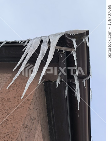 Icicles of ice hang from the downspout of the corner of the house's roof 136707669