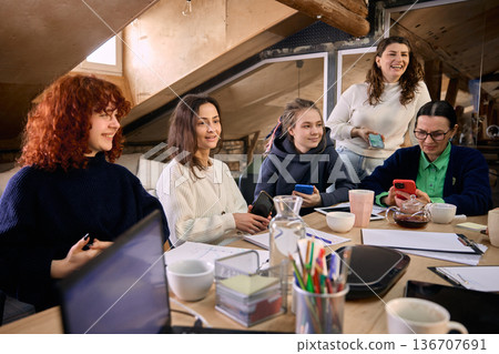 Female team gathered around table reviewing online campaign results. Female team gathered around table reviewing online campaign results. 136707691