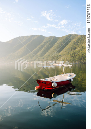 A serene red boat peacefully floating on calm waters surrounded by mountains in early morning light 136707718