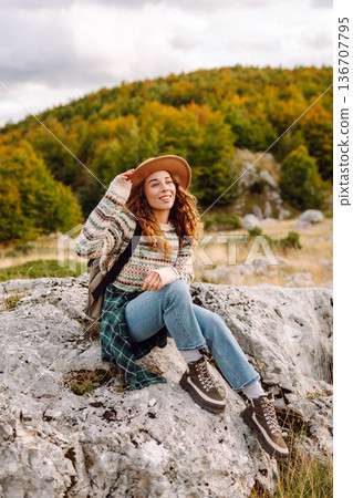 Young woman enjoys sunny afternoon in mountains while sitting on rocks. Tourism. Active lifestyle. 136707795
