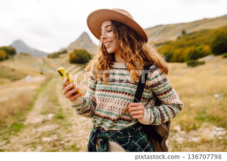 Woman is seen smiling, holding yellow phone in autumn landscape. Enjoying fresh air after hiking. Woman is seen smiling, holding yellow phone in autumn landscape. Enjoying fresh air after hiking. 136707798