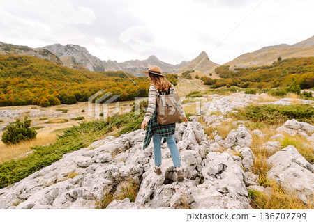 Back view. Travel woman explores scenic mountain landscape during in open field. Enjoying mountains Back view. Travel woman explores scenic mountain landscape during in open field. Enjoying mountains 136707799