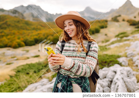 Woman is seen smiling, holding yellow phone in autumn landscape. Enjoying fresh air after hiking. Woman is seen smiling, holding yellow phone in autumn landscape. Enjoying fresh air after hiking. 136707801