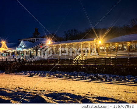 View of a coastal illuminated cafe from the frozen shore in winter at sunset 136707988