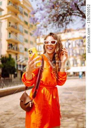Bright orange dress worn by a woman enjoying sunny day while taking selfie in a picturesque setting Bright orange dress worn by a woman enjoying sunny day while taking selfie in a picturesque setting 136708052
