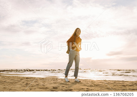Woman enjoying breezy day near vibrant red lighthouse at sunset. Travel, weekend, lifestyle concept. Woman enjoying breezy day near vibrant red lighthouse at sunset. Travel, weekend, lifestyle concept. 136708205