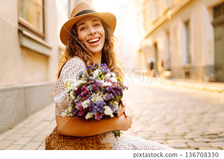 Beautiful young woman in summer style outfit smiling happy walking with flowers in city street Beautiful young woman in summer style outfit smiling happy walking with flowers in city street 136708330