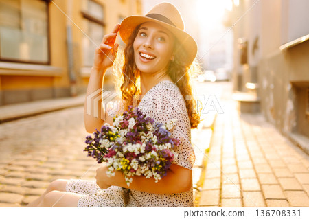 Beautiful young woman in summer style outfit smiling happy walking with flowers in city street Beautiful young woman in summer style outfit smiling happy walking with flowers in city street 136708331