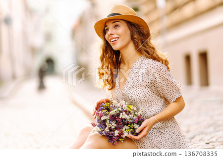 Happy young woman with a bouquet of wild flowers walks on the street city. Emotions. Fashion style Happy young woman with a bouquet of wild flowers walks on the street city. Emotions. Fashion style 136708335