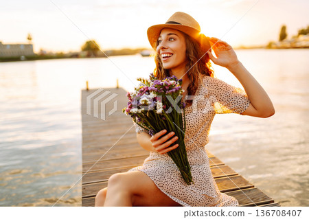 Young woman in dress sitting on wooden pier near pond. Rustic style of wedding. Travel, tourism Young woman in dress sitting on wooden pier near pond. Rustic style of wedding. Travel, tourism 136708407