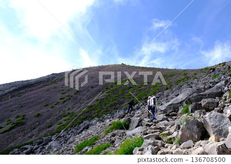 登山者攀登陡峭的岩石斜坡，背景是藍天白雲的高山景色（展現挑戰與努力的畫面） 136708500