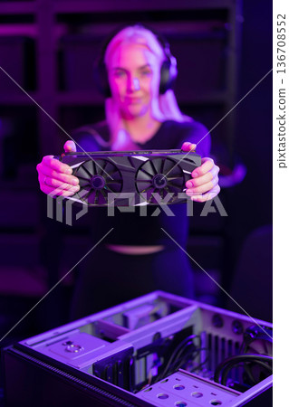 Female gamer in her 20s upgrades a gaming PC with high-end graphics card in neon-lit setup Female gamer in her 20s upgrades a gaming PC with high-end graphics card in neon-lit setup 136708552