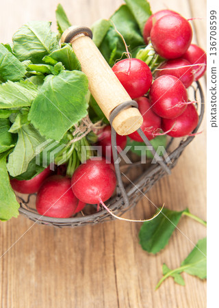 Fresh red radishes with green leaves in basket on wood 136708599