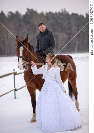 Bride Touching Horse While Groom Rides In Snow Bride Touching Horse While Groom Rides In Snow 136708707