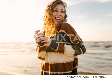 Portrait of a beautiful woman on the beach at sunset. Girl walks along the beach and enjoys weather Portrait of a beautiful woman on the beach at sunset. Girl walks along the beach and enjoys weather 136708718