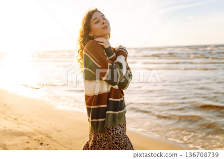 Portrait of a beautiful woman on the beach at sunset. Girl walks along the beach and enjoys weather 136708739