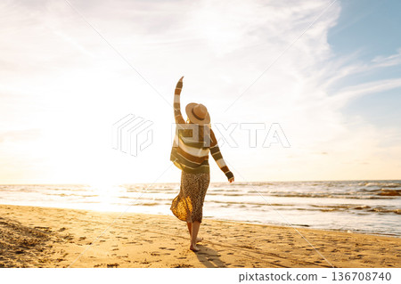 Beautiful woman at the windy spring day relaxing on coast. Carefree lady looking at the sunset. 136708740
