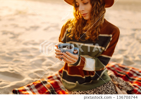Young happy traveler tourist sits at picnic on the beach drinks hot drink. People, journey concept 136708744
