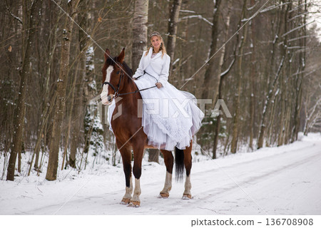 Bride Smiling While Riding Horse Through Winter Woods 136708908
