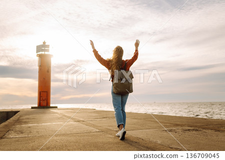Young woman enjoying a breezy day near a vibrant red lighthouse. Autumn sunset 136709045