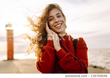 Young woman enjoying a breezy day near a vibrant red lighthouse. Autumn sunset Young woman enjoying a breezy day near a vibrant red lighthouse. Autumn sunset 136709046
