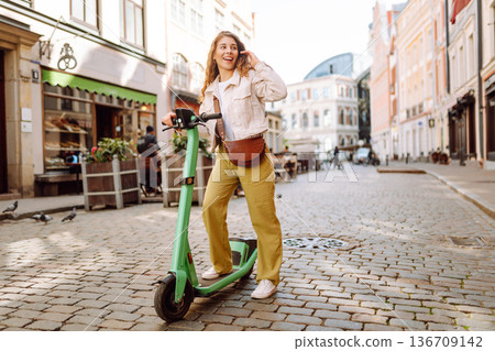 Beautiful woman riding an electric scooter. Street-style, Ecological transport. Active lifestyle. Beautiful woman riding an electric scooter. Street-style, Ecological transport. Active lifestyle. 136709142