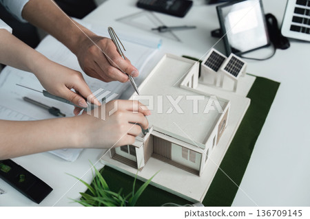Two people are working on a model of a house Two people are working on a model of a house 136709145
