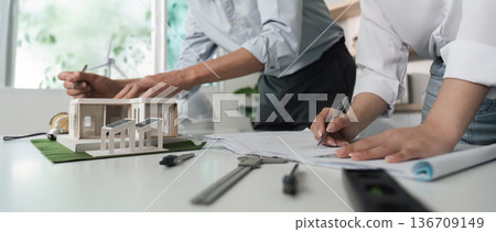 Two people are working on a drawing of a house 136709149