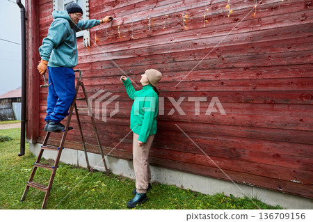 Villagers adorn house for Christmas hanging garland along walls. 136709156