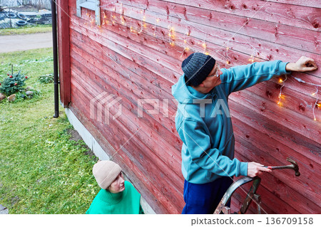 On Christmas eve married couple decorates facade of country house. 136709158