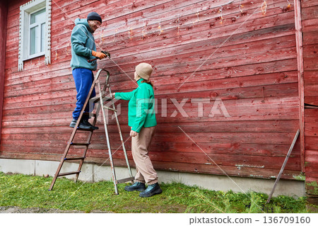Getting ready for Christmas married couple adorns wooden house with festive decor. 136709160