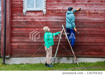 Installing string lights on facade of wooden farm building. Installing string lights on facade of wooden farm building. 136709162