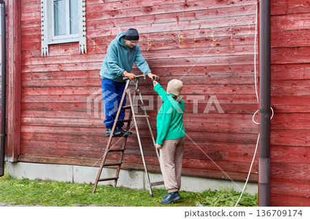 Decorating farm building for Christmas couple hangs garland on exterior. 136709174
