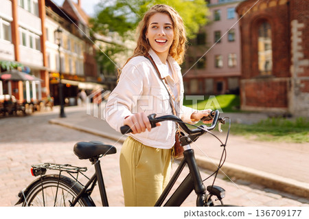 Woman using mobile phone, walks with bicycle, looks around at beautiful architecture. Selfie time. 136709177