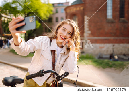 Woman using mobile phone while walks with a bicycle. Selfie time. People, blogging and lifestyle. 136709179